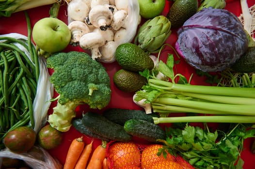 A colorful assortment of fresh vegetables including broccoli, carrots, and avocados, arranged on a red backdrop. Perfect for promoting healthy eating, vegetarian lifestyles, and organic produce.