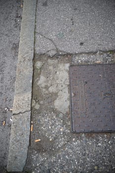 Cremona, Italy - November 15th 2024 Close-up view of a manhole cover and curb on a city street, revealing disrepair and scattered cigarette butts