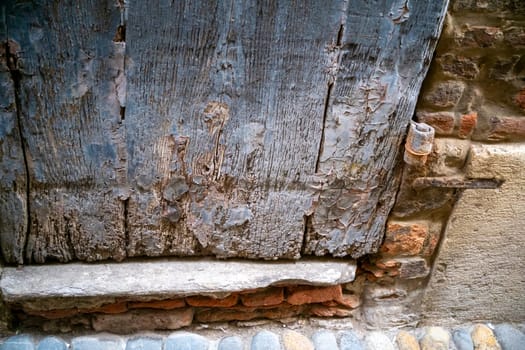 Cremona, Italy - November 15th 2024 Close-up of a weathered wooden door with peeling paint, highlighting the effects of time and decay in a historical context