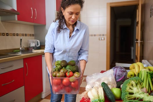 A woman arranges an assortment of fresh vegetables in a bright, modern kitchen. The scene captures a sense of healthy living and organization, highlighted by colorful produce and a clean environment.