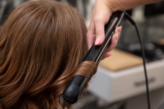 A highly skilled stylist expertly utilizes a hair straightener to craft beautiful and stunning curls on a clients hair