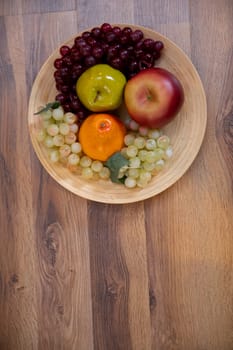 A beautifully vibrant and colorful mix of grapes, apple, orange, and green apple sits in a wooden bowl on a table