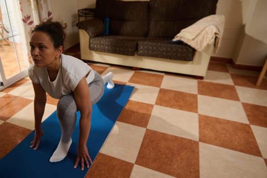 A woman focuses on her yoga session in a cozy living room. Her determination and tranquility highlight the commitment to a healthy lifestyle and mindful exercise.