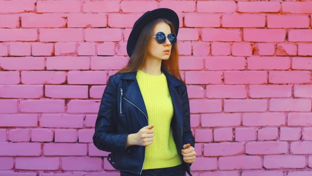 Fashion, trendy, stylish young woman in black round hat, leather jacket, yellow sweater looking away, modern girl posing on colorful pink wall background