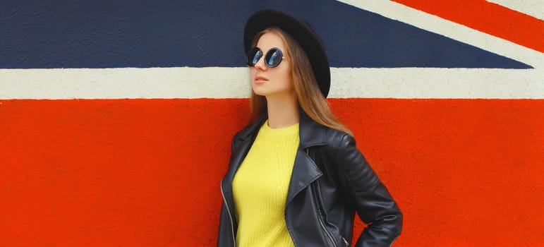 Fashion, trendy, stylish young woman in black round hat, leather jacket, yellow sweater looking away, modern girl posing on colorful background