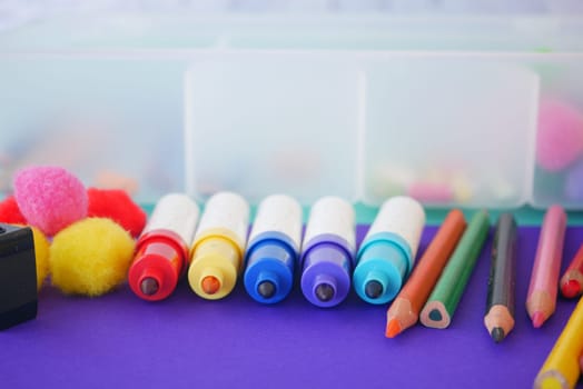 Vibrant markers, colorful pencils, and fluffy pompoms are arranged to inspire creativity