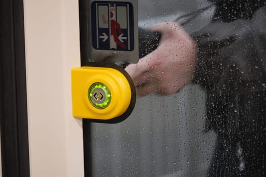 finger presses button to open doors in subway car