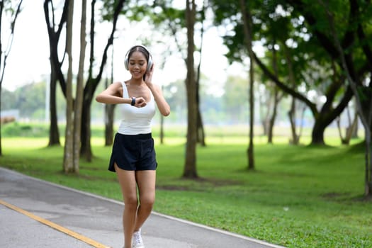 Smiling young woman checking her fitness data on smartwatch while jogging in a park.