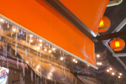 An orange canopy overhead draped in gentle rain, with lanterns and soft lights creating warmth