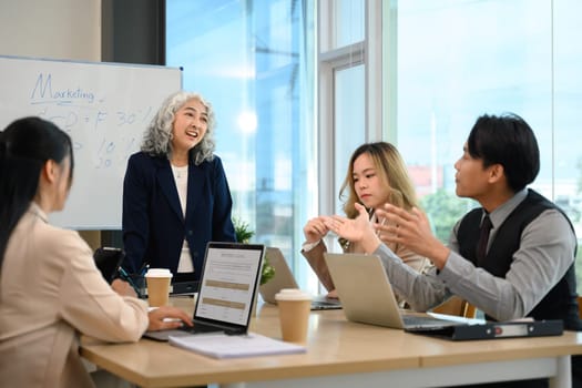 Mature executives businesswoman explaining a strategy on whiteboard during meeting.
