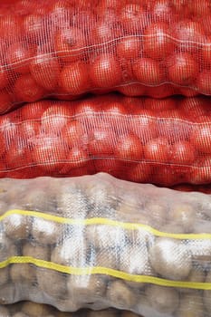 A variety of fresh bags filled with red onions, potatoes, and assorted vegetables are stacked