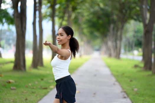 Young woman in sportswear warming up her body preparing for workout in serene park.