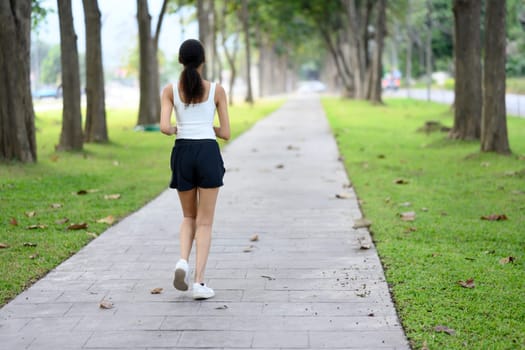 Young sportswoman jogging on a paved path through a park.