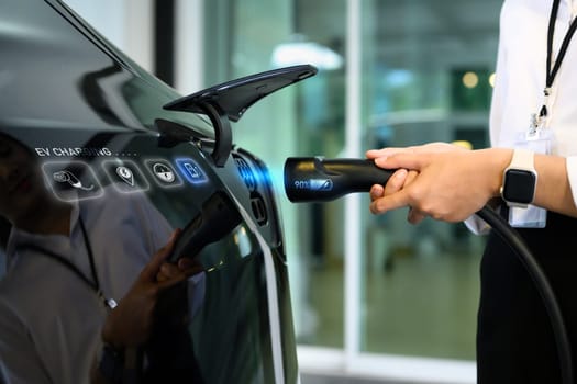 Closeup woman plugging electric car from charging station. Alternative energy and transportation concept.