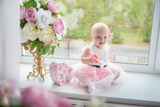 A little girl plays on a window sill surrounded by flowers and a decorative box.