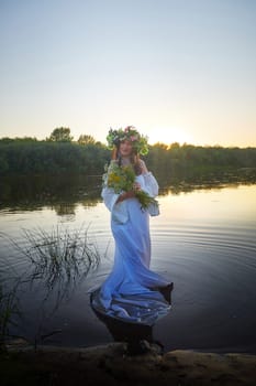 Slavic plump chubby girl in long white dress on the feast of Ivan Kupala with flowers and water in a river or lake on summer evening