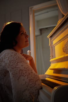 A woman in a delicate dress sits beside a piano, lost in thought as warm light enhances the romantic atmosphere of the setting.