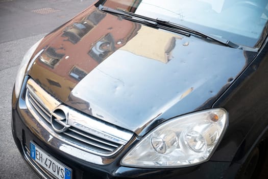 Cremona, Lombardy, Italy - October 27th 2024 Parked black opel zafira reflecting a building on its slightly damaged hood
