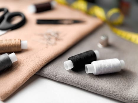 Sewing essentials with thread spools, needles, and measuring tape on fabric background.