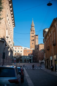 Cremona, Italy - November 27th 2024 View of the torrazzo bell tower of cremona cathedral rising above a quiet street with parked cars and pedestrians in the city center