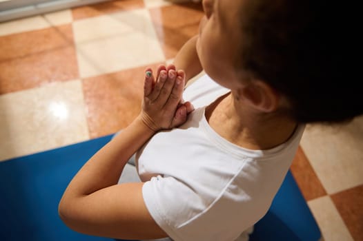 A woman in a white shirt practices yoga indoors on a blue mat, focusing on meditation. The pose suggests peace and mindfulness, creating a serene and calming atmosphere.