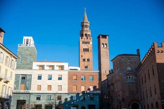 Cremona, Italy - November 27th 2024 Cremona cathedral's torrazzo, the tallest pre-modern brick tower in europe, dominates the skyline amidst other historic buildings under a vibrant blue sky