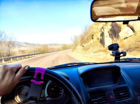 Car salon, windshield, hand of woman on steering wheel and landscape. View from seat of driver on nature landscape. Single trip of female traveler