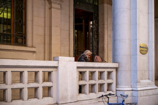 Cremona, Italy - November 27th 2024 Senior woman resting on the railing outside the central post office in cremona, italy