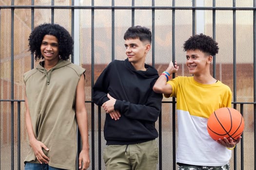 three multiracial male teenagers with basketball smiling happy together on street, concept of friendship and urban lifestyle
