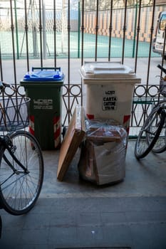 Cremona, Italy - November 27th 2024 Glass and paper separate waste collection bins and some cardboard packaging left on the ground in cremona, italy