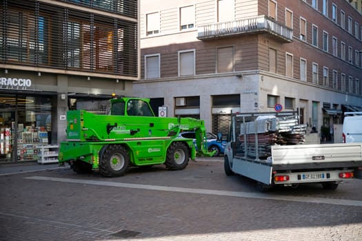 Cremona, Lombardy, Italy - October 27th 2024 A green merlo roto telehandler is parked next to a small truck loaded with scaffolding