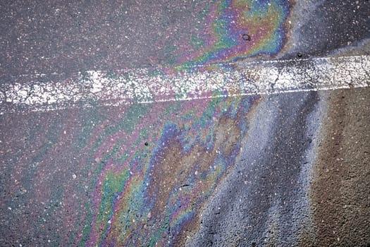 Oil spill on wet asphalt, parking lot with dividing line.