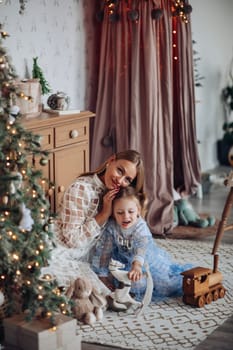 Smiling girl with mom near christmas tree at home.