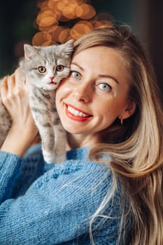 A beautiful woman at home near the Christmas tree with her beloved pet cat.