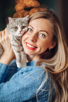A beautiful woman at home near the Christmas tree with her beloved pet cat.
