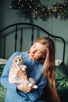 A beautiful woman at home near the Christmas tree with her beloved pet cat.