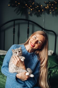 A beautiful woman at home near the Christmas tree with her beloved pet cat.