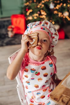 .a girl child in the kitchen with a Christmas tree is preparing or cooking ginger cookies for Christmas or New year