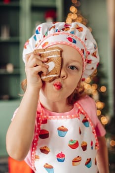 .a girl child in the kitchen with a Christmas tree is preparing or cooking ginger cookies for Christmas or New year