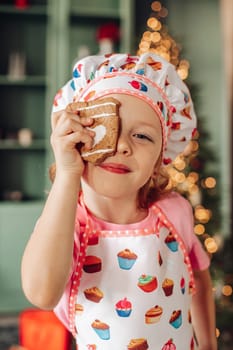 .a girl child in the kitchen with a Christmas tree is preparing or cooking ginger cookies for Christmas or New year