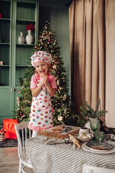 .a girl child in the kitchen with a Christmas tree is preparing or cooking ginger cookies for Christmas or New year
