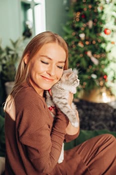 A beautiful woman at home near the Christmas tree with her beloved pet cat.