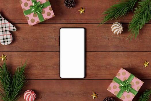 Flat lay image of a smartphone mockup on a wooden table with wrapped gifts and Christmas ornaments, perfect for holiday design projects.
