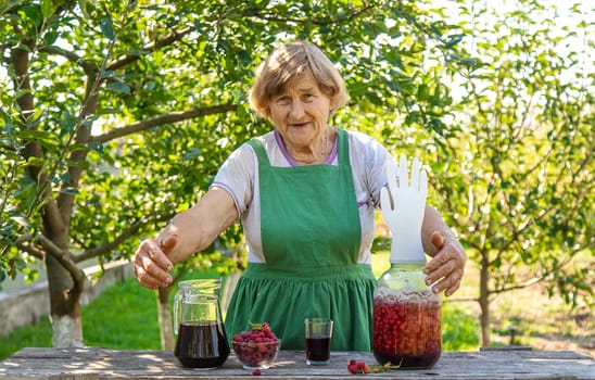 Grandma makes wine from raspberries in the garden. Selective focus. drink.