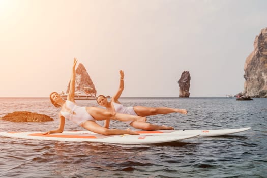 Woman sup yoga. Middle age sporty woman practising yoga pilates on paddle sup surfboard. Female stretching doing workout on sea water. Modern individual hipster outdoor summer sport activity