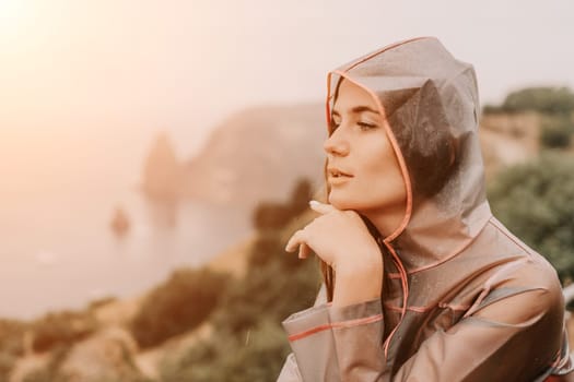 Woman rain park. Happy woman portrait wearing a raincoat with transparent umbrella outdoors on rainy day in park near sea. Girl on the nature on rainy overcast day