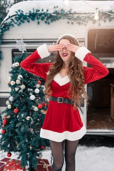 Young woman in santa costume decorates the Christmas tree at winter campsite getting ready for the new year. New year celebration concept