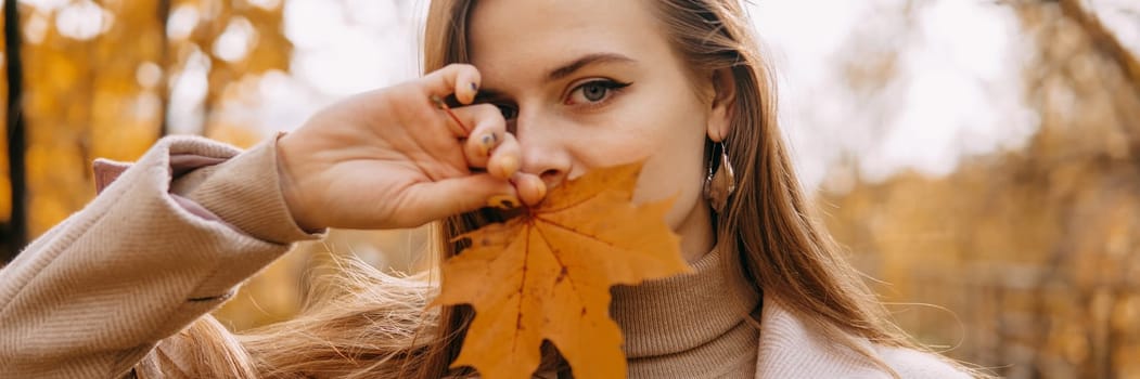 Portrait of a woman with an autumn maple leaf. Railway, autumn leaves, a young long-haired woman in a light coat coat, close-up.