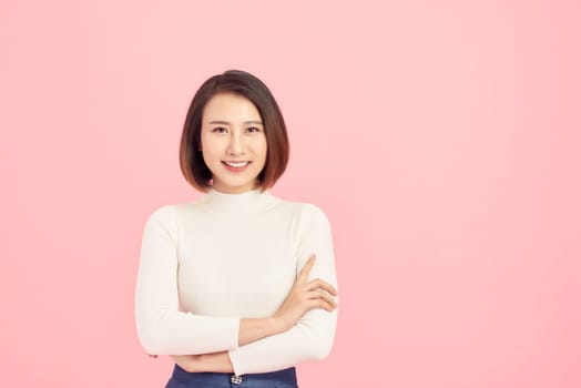 Young Asian woman wearing  sweater standing over isolated pink background happy face smiling with crossed arms looking at the camera. Positive person.