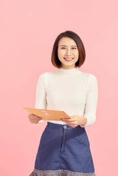asian business woman smiling and holding document binders, pink background.